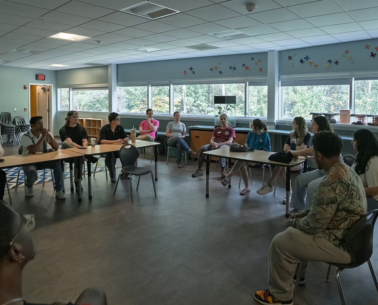 Museum staff and our design team seated in a circle of chairs and tables in a bright classroom at the Museum of Life and Science, talking through the conservatory.