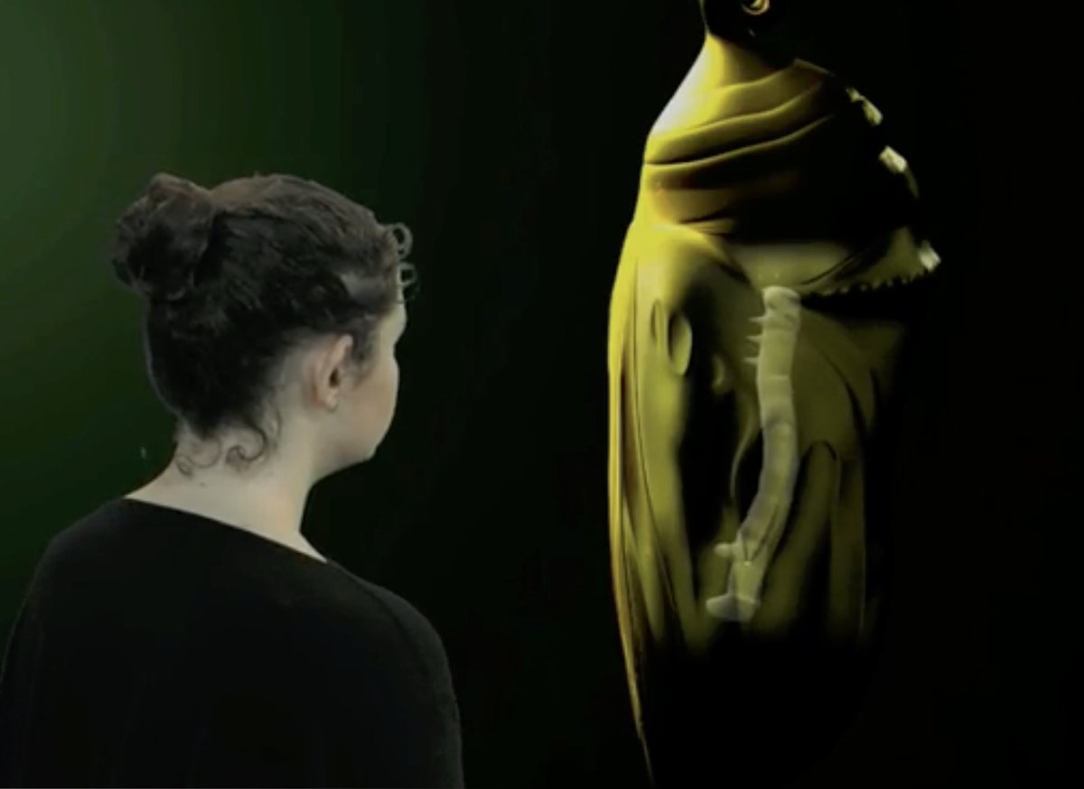 A visitor looks up at a giant glowing yellow chrysalis in the dark Chrysalis Room.